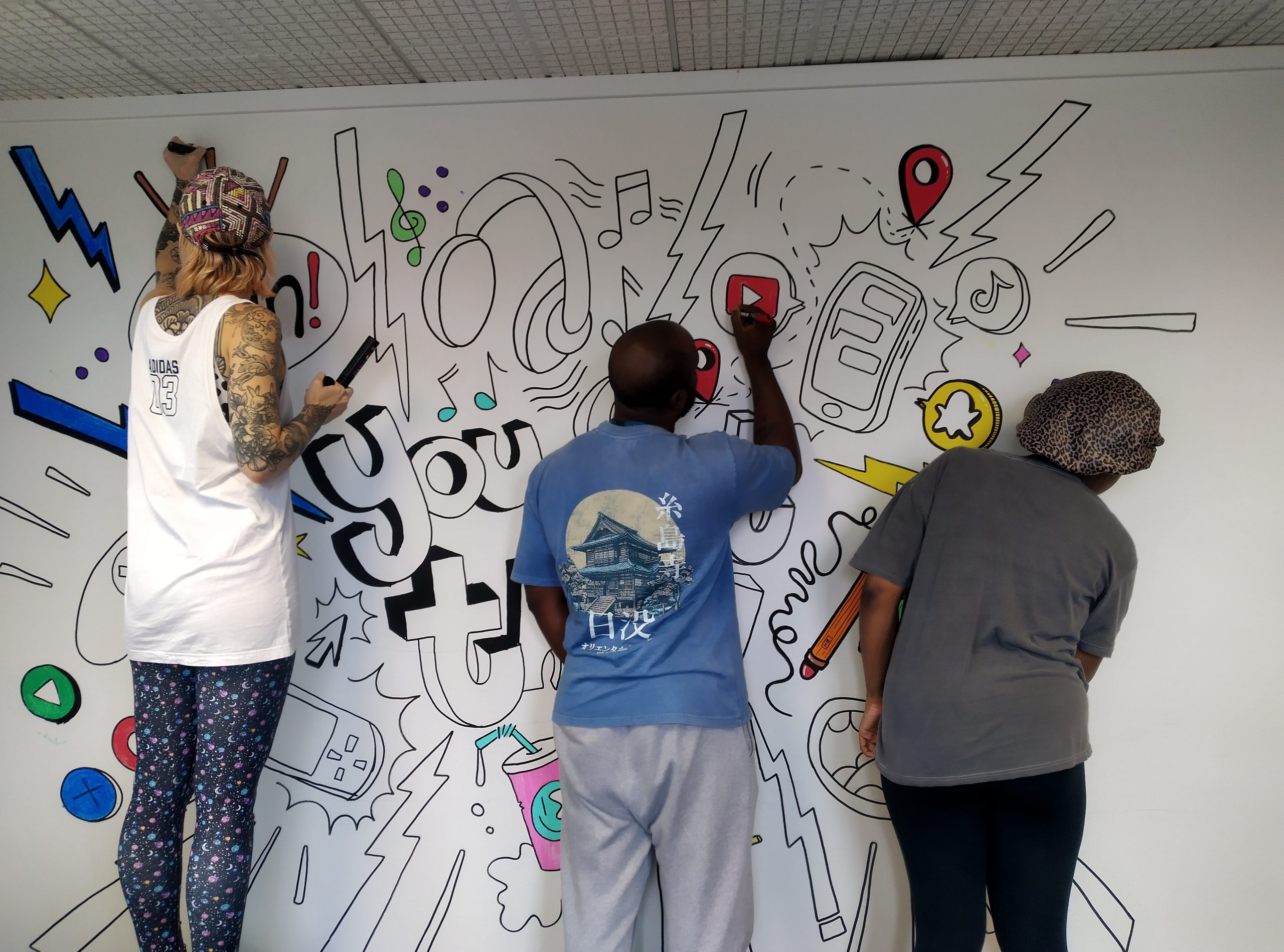 Three young people drawing a mural on a wall